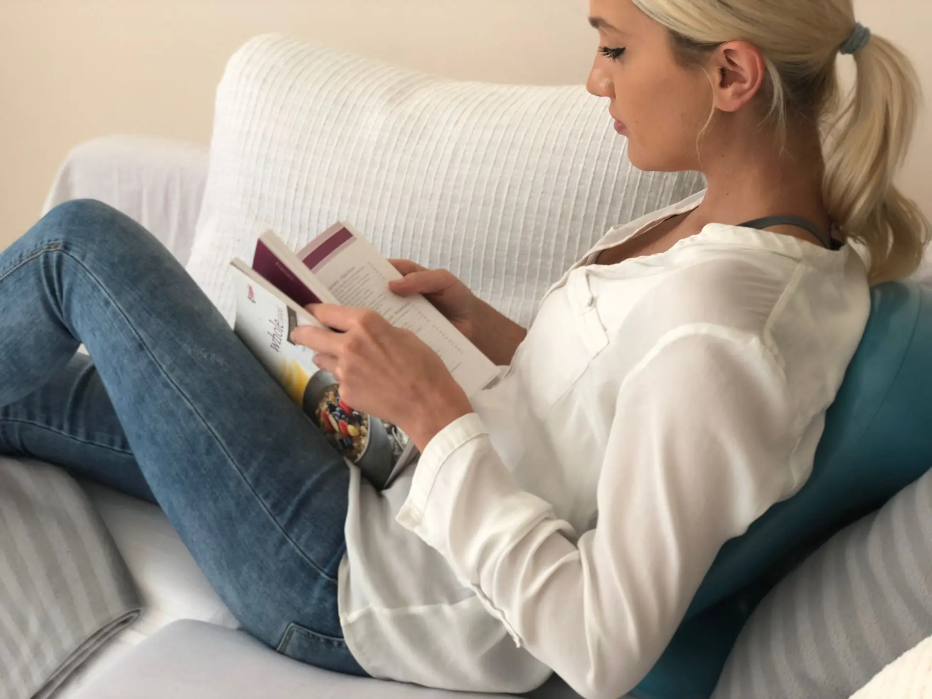 Woman reading a book at home on a couch lying on an Air8 Cushion